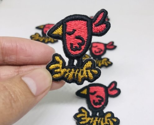a hand picking up extra small sized artistic bird embroidery patch with heat seal backing on white background